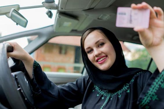 Mujer musulmana conduciendo un coche, sosteniendo una licencia.