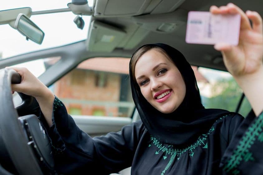 Mujer musulmana conduciendo un coche, sosteniendo una licencia.