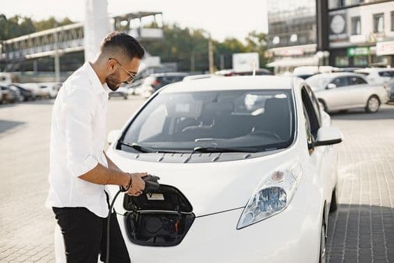 Hombre árabe joven cargando un coche eléctrico blanco.