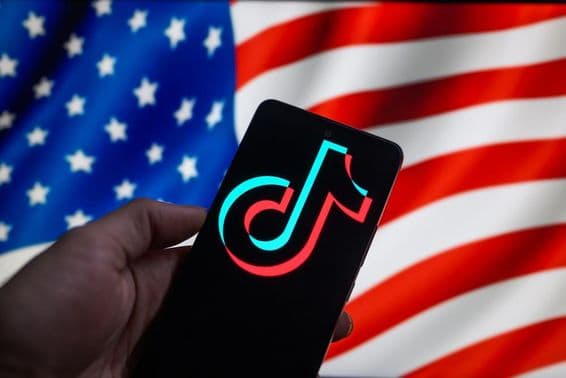 El logotipo de TikTok mostrado en un smartphone con la bandera de EE.UU al fondo.