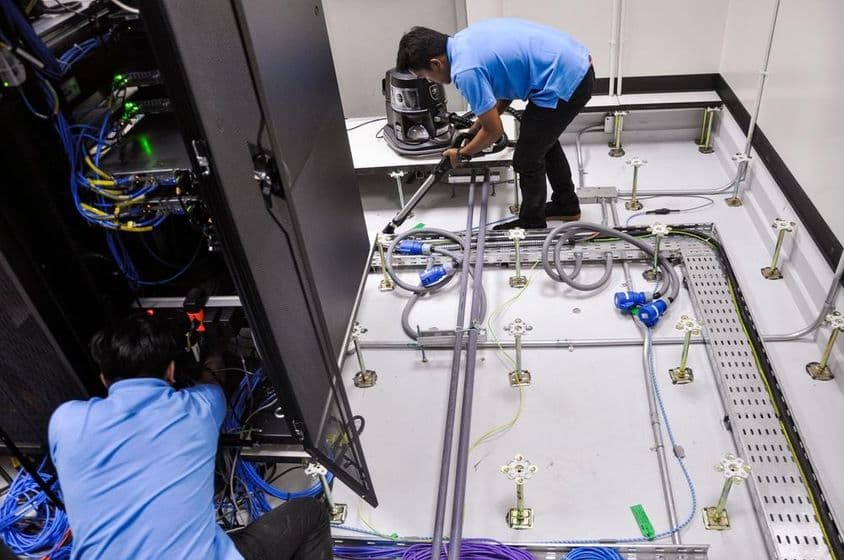 Trabajadores construyendo una sala de servidores, piso elevado y gabinetes de rack.