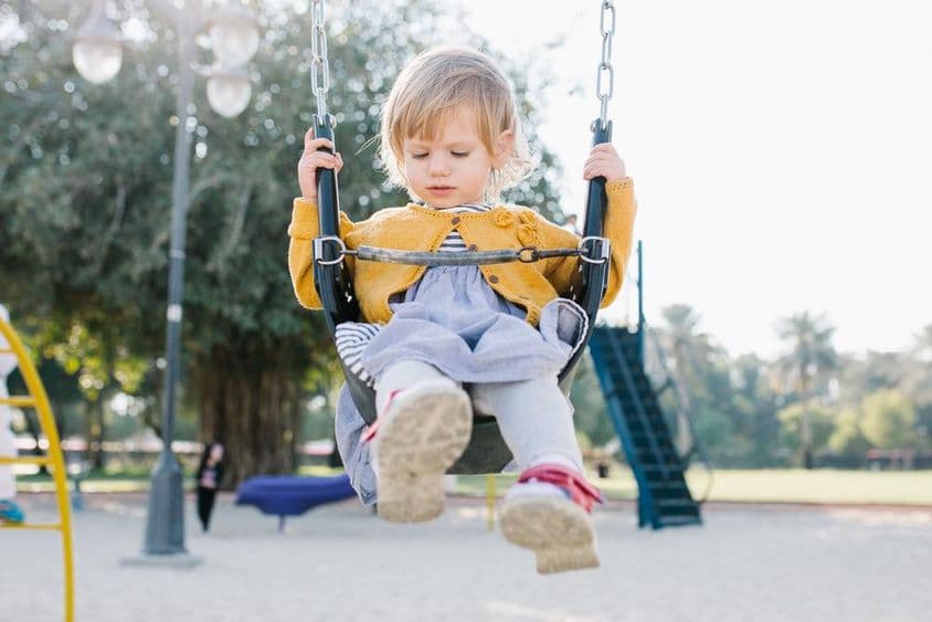 Niña pequeña feliz columpiándose en el parque bajo el sol.