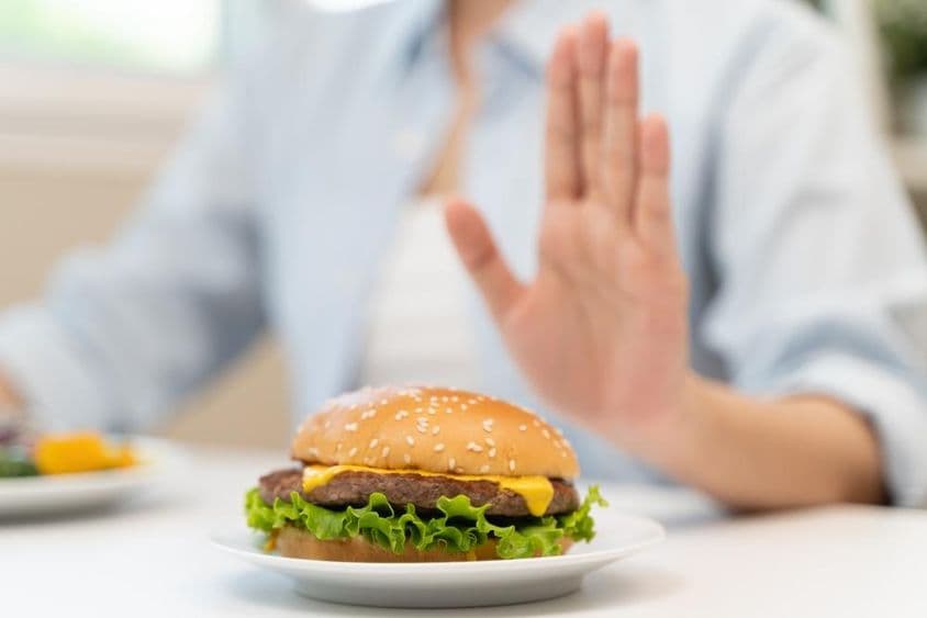 Una mujer rechaza una hamburguesa de comida rápida alta en grasas.