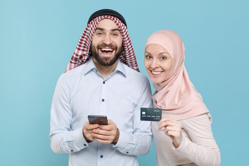 Pareja sonriente sosteniendo tarjeta de crédito y teléfono.