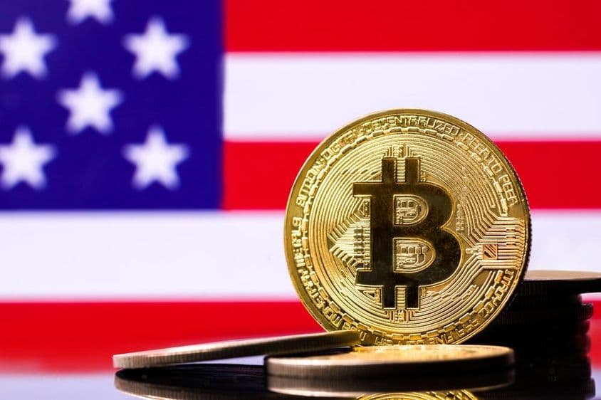 Moneda de metal Bitcoin dorada con la bandera de EE.UU. de fondo.