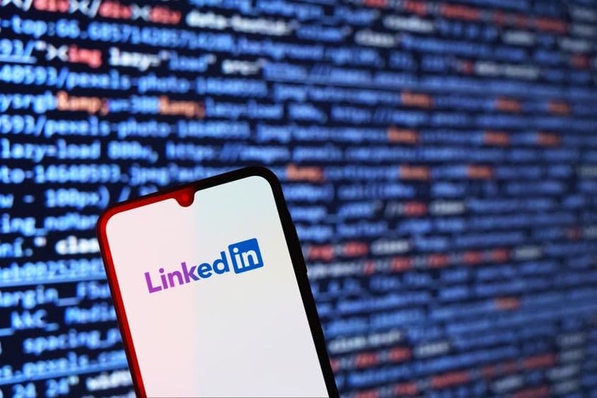 Smartphone mostrando el logotipo de LinkedIn con fragmento de código al fondo.