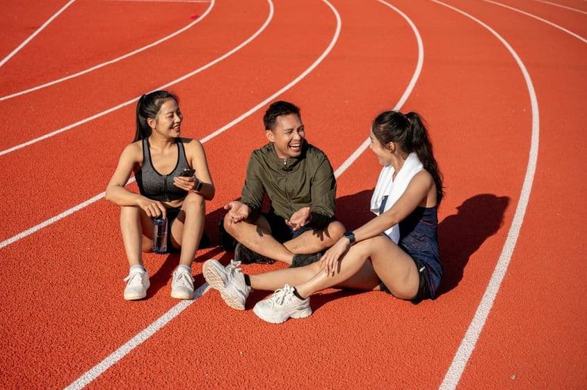 Un grupo de atletas alegres descansando en un campo deportivo bajo el sol después del entrenamiento.