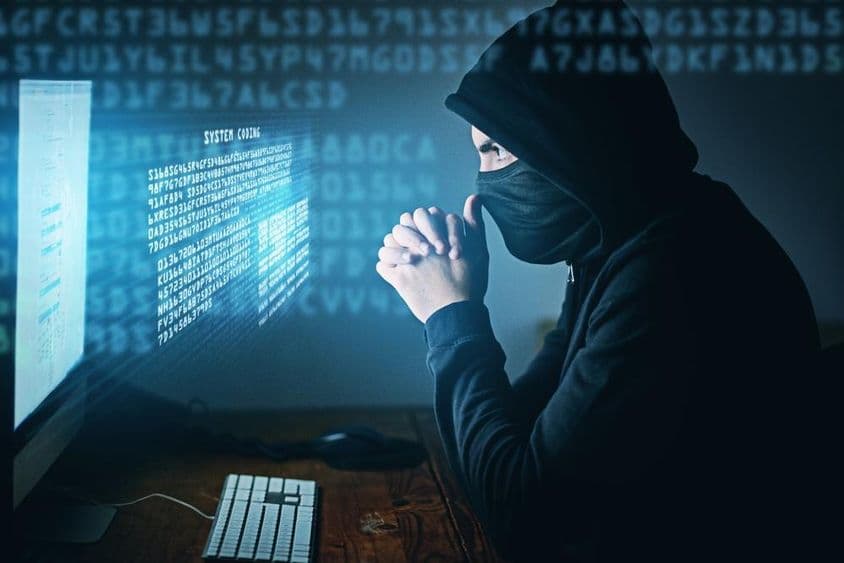 Cibercrimen, hombre encapuchado frente a una computadora.