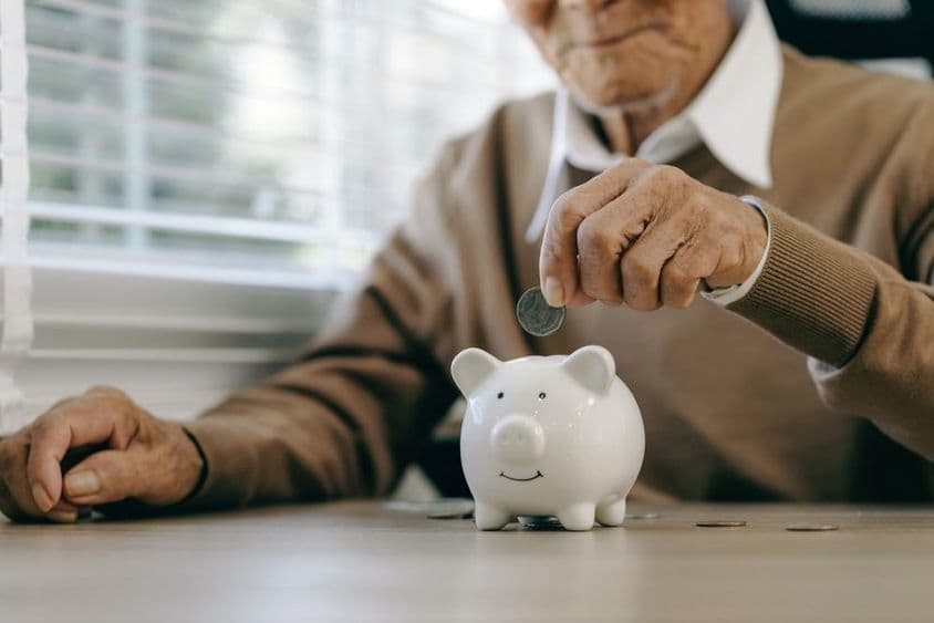 Ahorrar dinero, anciano colocando monedas en una alcancía