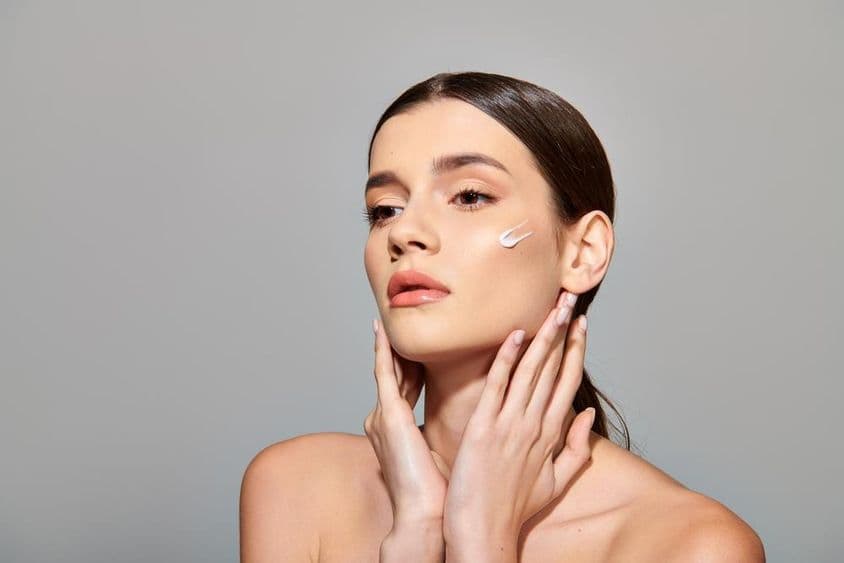 Una joven de cabello castaño aplicando una crema de belleza en su rostro, exudando una sensación de autocuidado.
