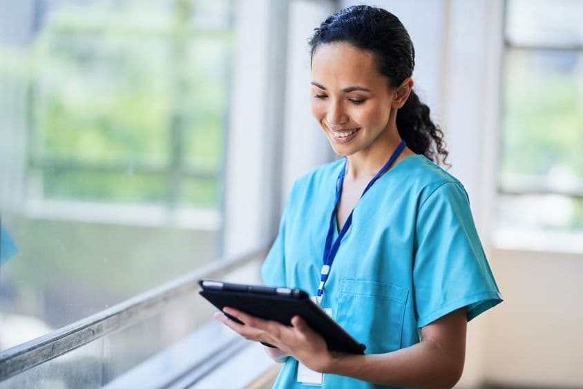 Enfermera sonriente con una tableta digital en una instalación médica moderna.