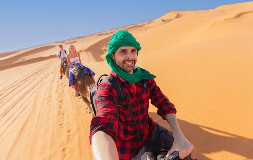 Una persona disfrutando de una salida grupal mientras monta un camello en el desierto.