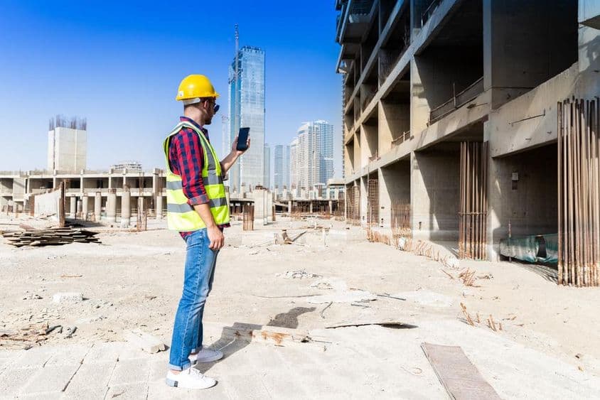 Teléfono inteligente, casco de construcción y chaqueta reflectante bajo el horizonte de Dubái, trabajador de la construcción.