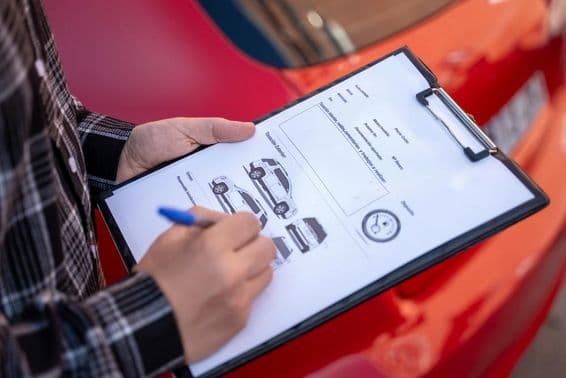 Un agente de seguros evalúa daños en un automóvil tras un accidente de tráfico, completando un formulario de reclamo de seguro.