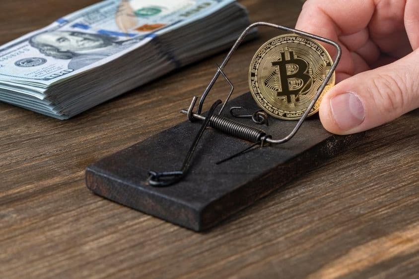 Monedas de criptomonedas Bitcoin en trampa para ratones, atrapadas con billetes de 100 dólares estadounidenses.