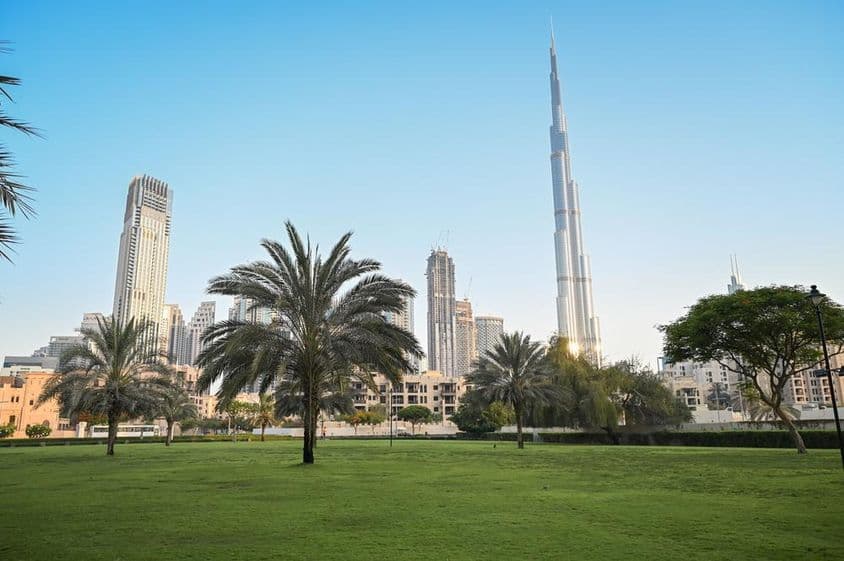 Dubái, Emiratos Árabes Unidos, parque verde en área residencial con Burj Khalifa al fondo.