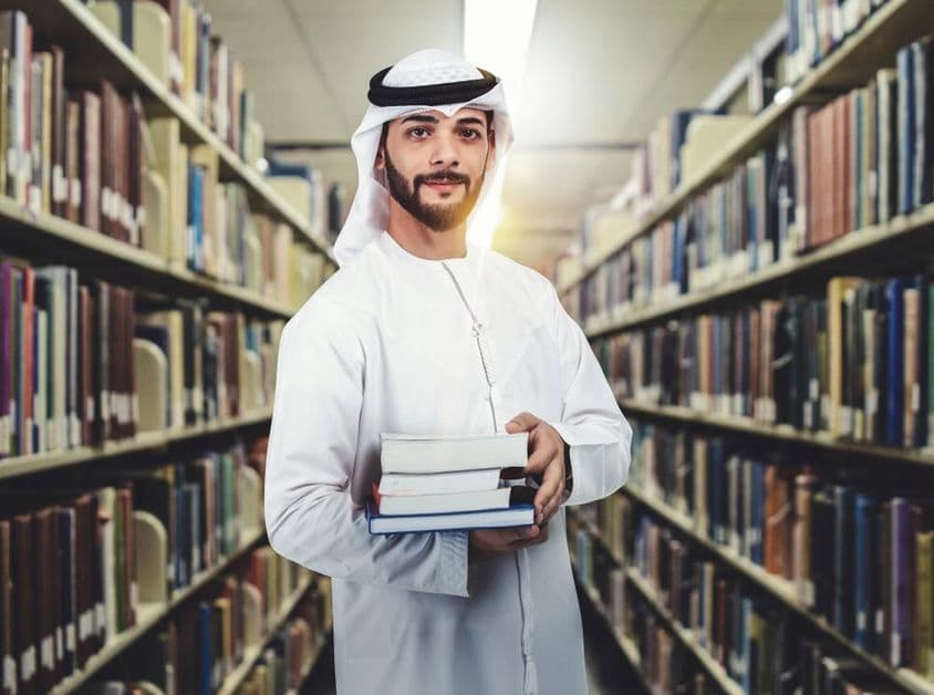 Estudiante árabe en biblioteca sosteniendo libros.