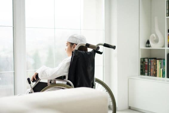 Un niño joven en silla de ruedas mirando por una ventana.