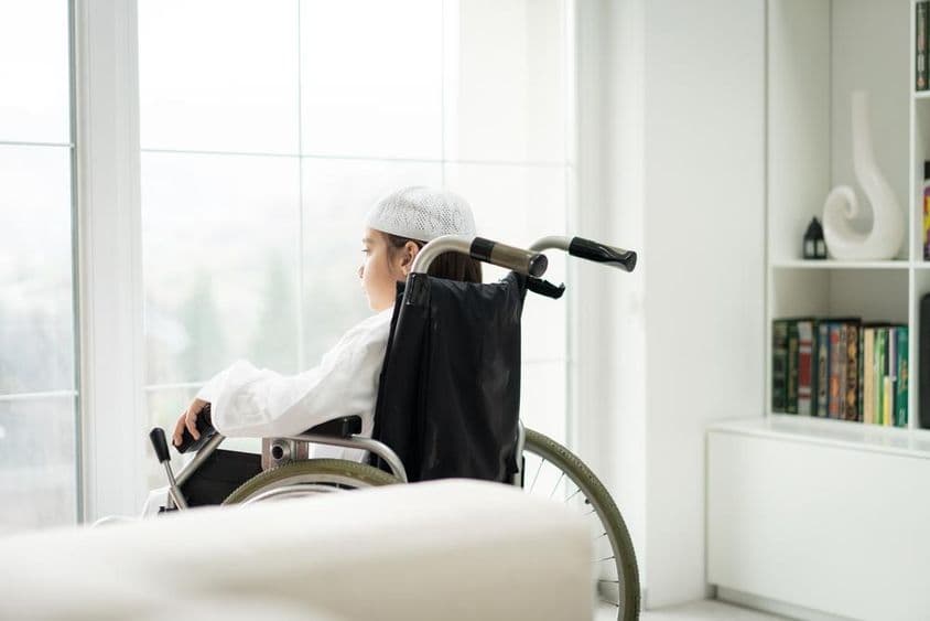 Un niño joven en silla de ruedas mirando por una ventana.
