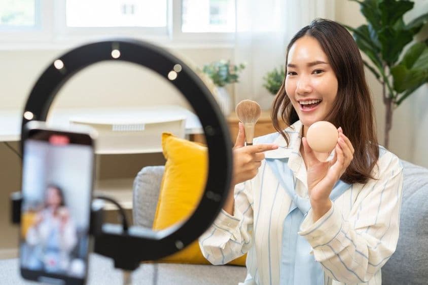 Influencer joven mujer bloguera usando teléfono inteligente hablando en un podcast de transmisión de video.