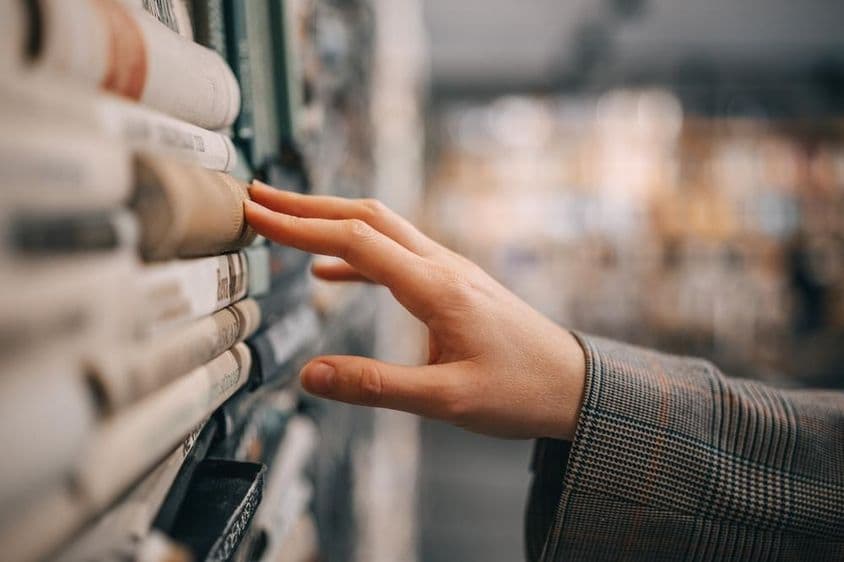 Una mano toca el lomo de un libro antiguo en una estantería.