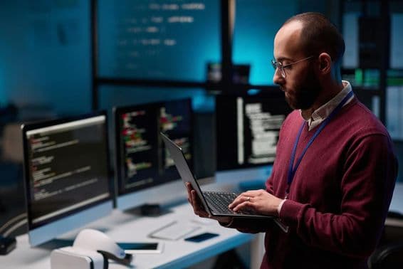 Programador informático sosteniendo un portátil abierto en una oficina de TI y ciberseguridad.