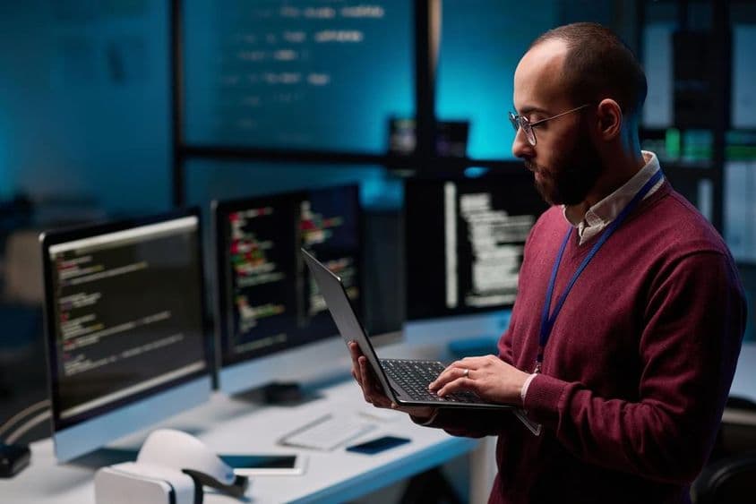 Programador informático sosteniendo un portátil abierto en una oficina de TI y ciberseguridad.