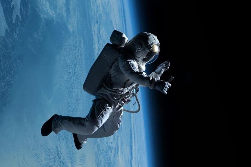 Astronauta femenina realizando una videollamada con su teléfono durante una caminata espacial en el espacio profundo.