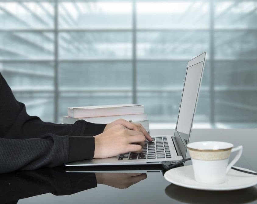 Una mujer trabajando en una laptop con una taza de café a su lado.