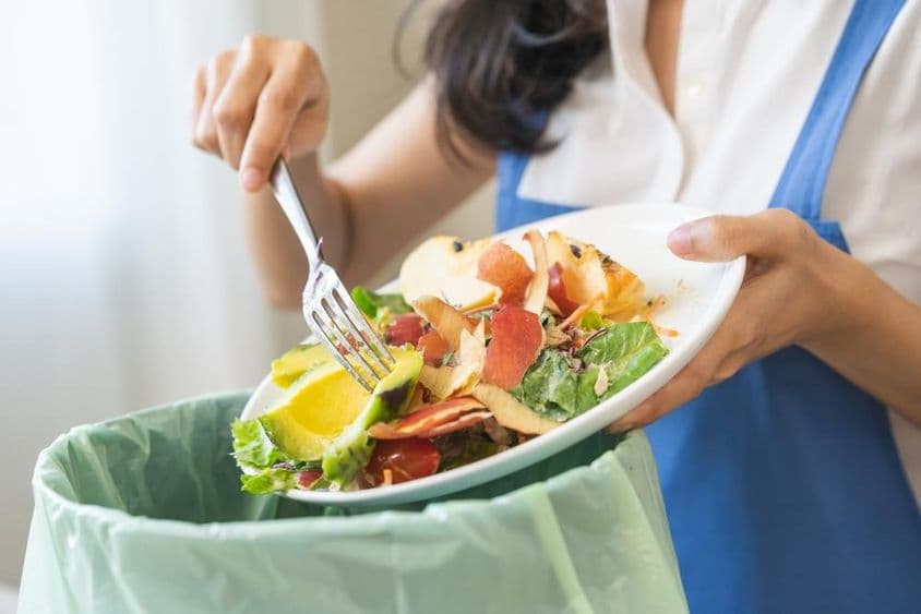 Compostaje de desperdicios alimentarios, joven ama de llaves raspando desperdicios con un tenedor.