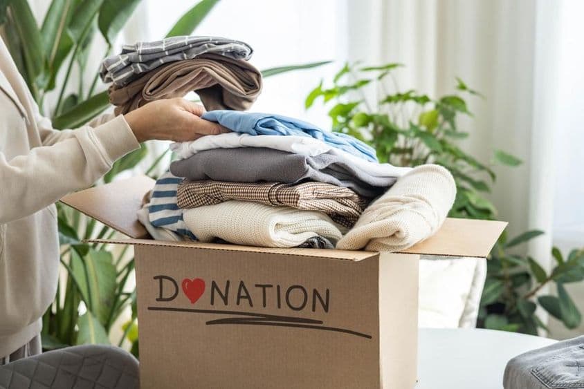 Una mujer en casa colocando ropa en una caja de cartón para donación, para reciclar.