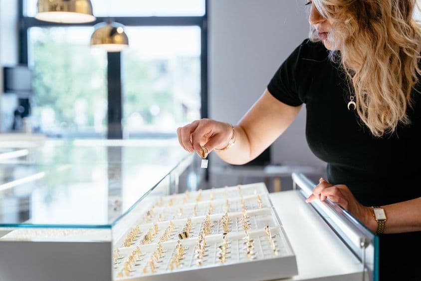 Una vendedora de joyas colocando un anillo de oro en el mostrador de la joyería