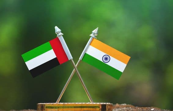 Banderas pequeñas de India y EAU contra un fondo verde difuminado.