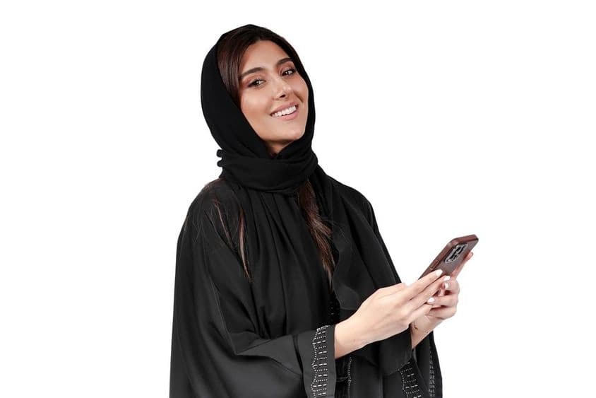 Empresaria emiratí en abaya árabe trabajando en un teléfono móvil.