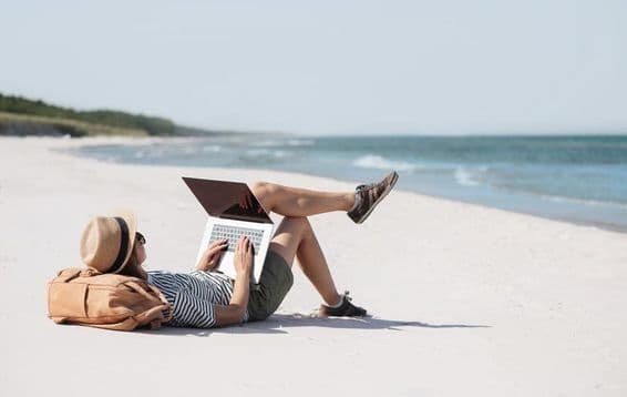 Una joven trabajando en una laptop junto al mar haciendo trabajo freelance.