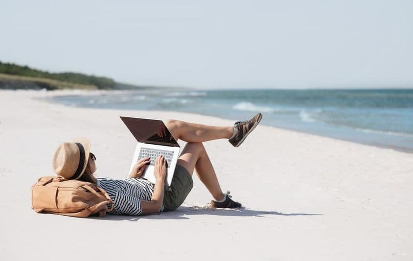 Una joven trabajando en una laptop junto al mar haciendo trabajo freelance.