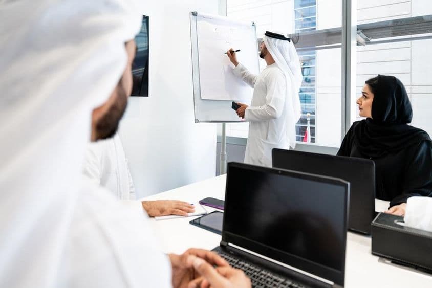 Un grupo de empresarios en atuendo tradicional emiratí teniendo una reunión en una oficina en Dubái.