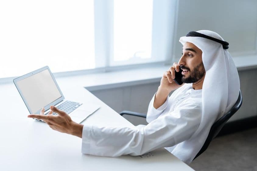 Un empresario exitoso en atuendo blanco tradicional emiratí trabajando en Dubái.