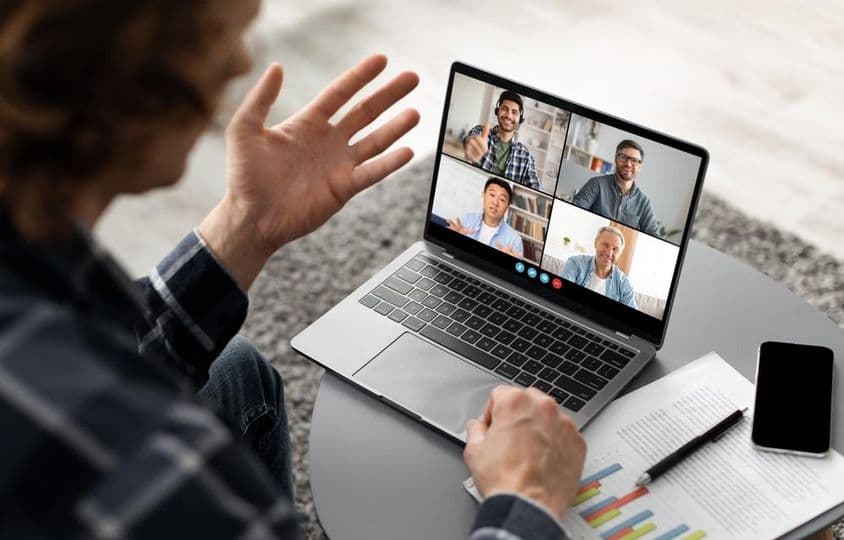 Un hombre sentado en un escritorio, participando en una videoconferencia en su portátil.