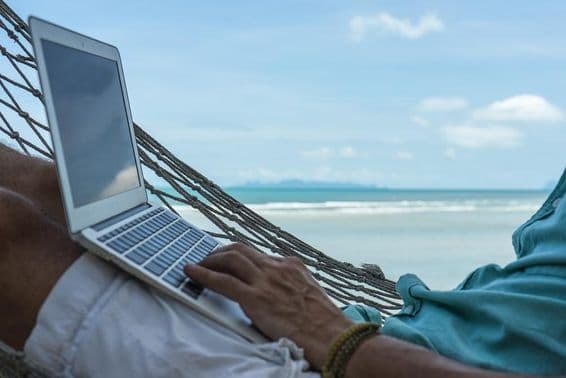 Un hombre trabajando en una computadora en una hamaca con una laptop en la playa de Dubái.