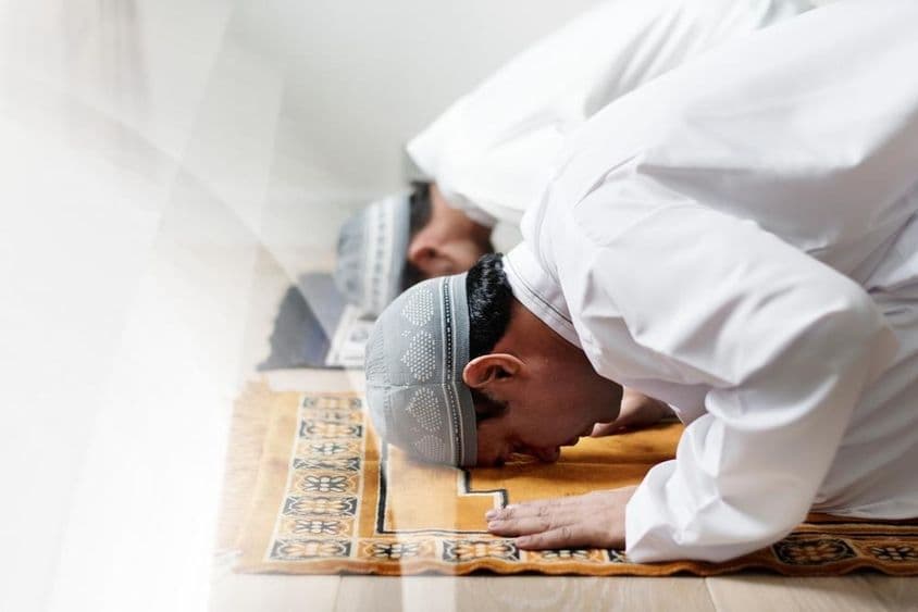 Hombres islámicos vestidos de blanco inclinándose en oración.