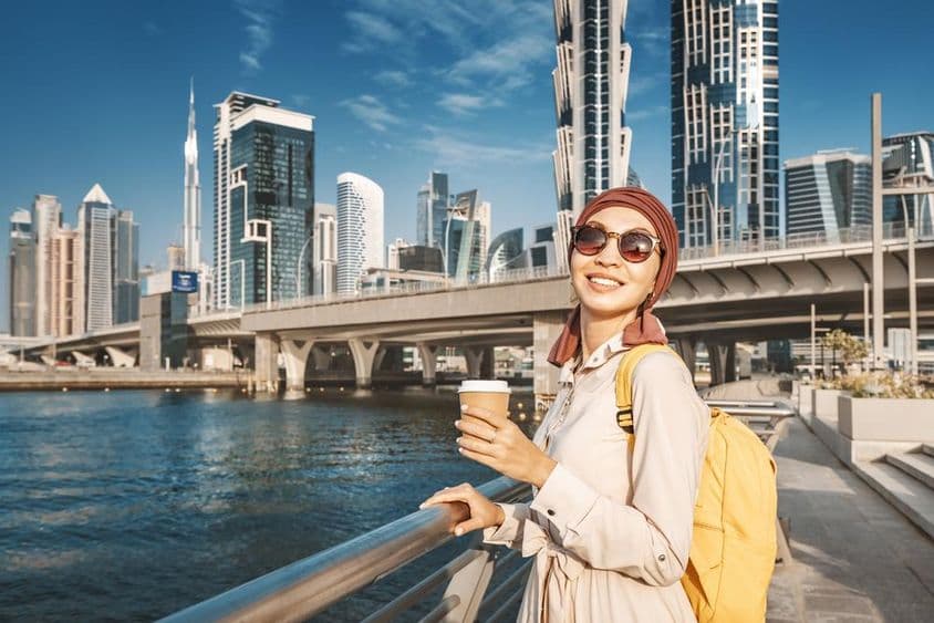 Mujer musulmana con mochila amarilla caminando por el canal de Dubái.