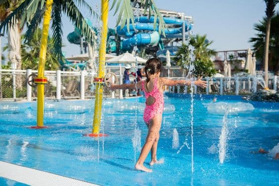 Niña pequeña jugando en una piscina con fuentes en un parque acuático.