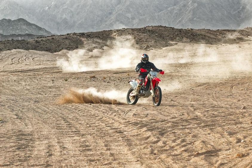 Motociclista con casco conduciendo en el desierto