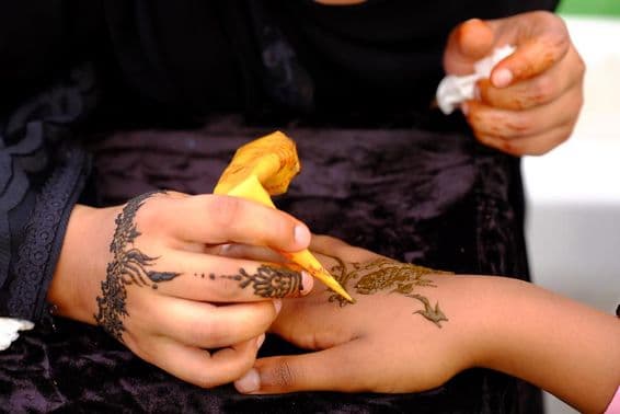 Una chica aplicando diseño de henna en la mano de otra.