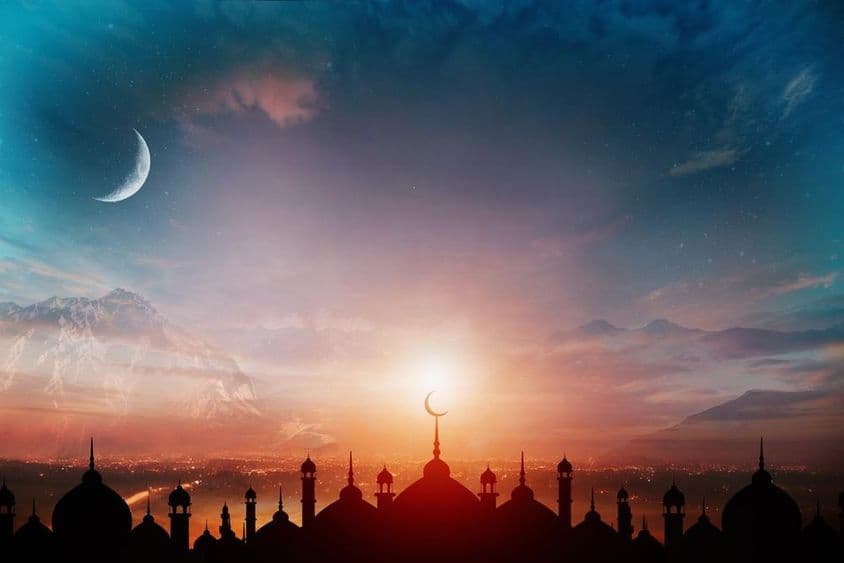 Cúpulas de mezquita contra un cielo azul crepuscular con una luna creciente al fondo.