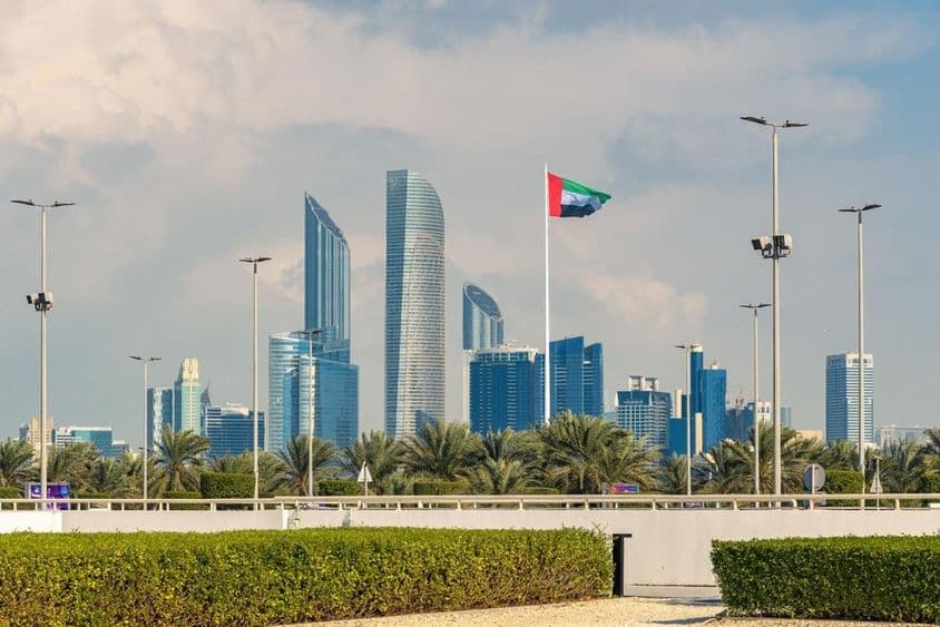 El icónico skyline de Abu Dabi con un rascacielos moderno y la bandera nacional prominente.