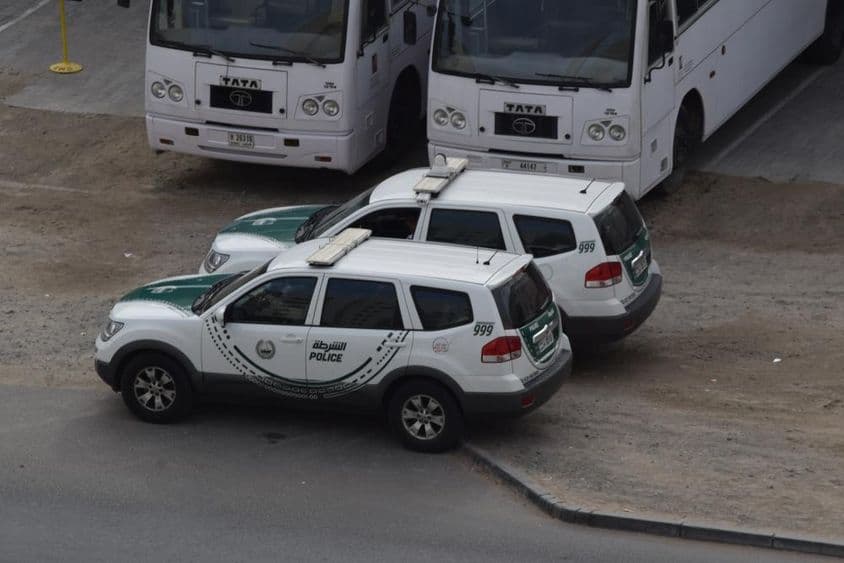 Dos coches de policía de Dubái estacionados frente a dos autobuses en Al Quoz, Dubái.