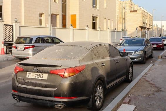 Coches con matrícula de Dubái polvorientos y arenosos estacionados en Abu Dhabi.