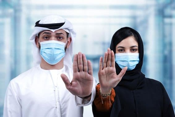 Hombre y mujer árabes con mascarillas médicas mostrando un gesto de detener.